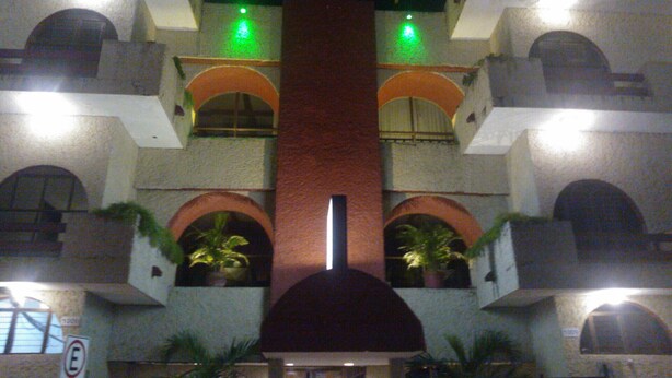 A multi-story building with a central red column, balconies with potted plants, and illuminated green lights. - Hotel y Restaurante Ritz de Tabasco (Villahermosa)