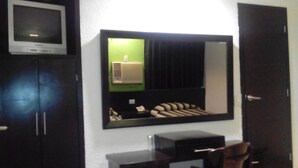 Una habitación con un espejo grande, un televisor sobre un mueble y una puerta.