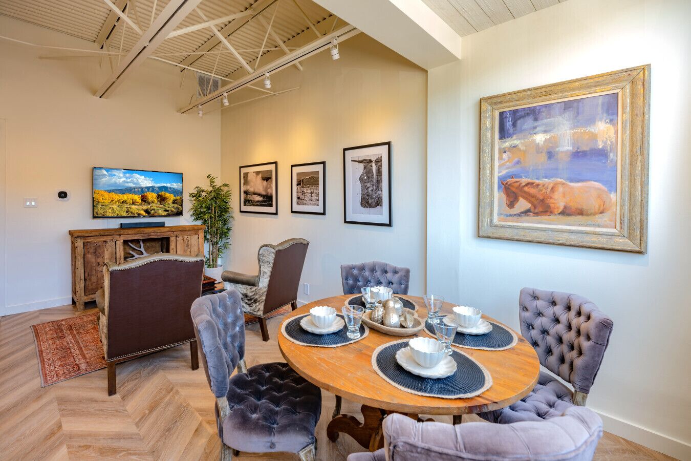 A dining area with a round wooden table, six upholstered chairs, and a large painting on the wall.