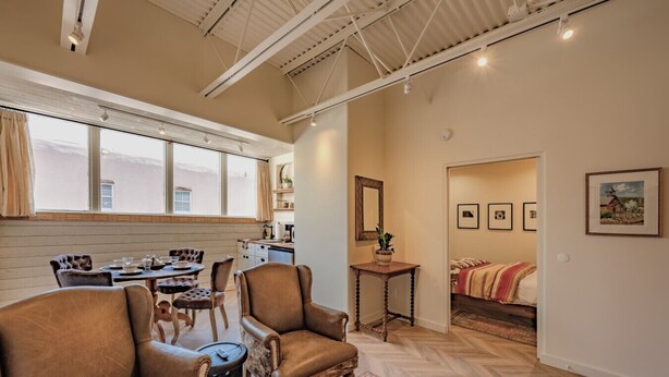 A spacious living area with leather armchairs, a dining table, and a kitchen in the background. - Bright & Spacious Loft at the Historic Plaza! - 375 Sq Ft (Santa Fe)