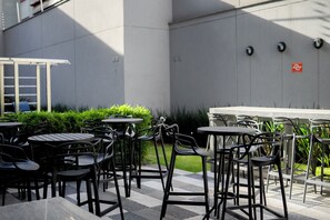 Outdoor seating with tables and chairs, a checkered floor, and a wall with a door and a small sign.