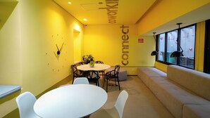 Ein gelbes Interieur mit rundem Tisch, Stühlen, einer Couch und einem Fenster mit Jalousien.