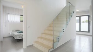 A modern interior with a curved staircase, a bed with patterned bedding, and a large window providing a view outside.