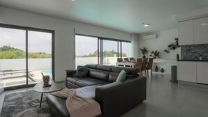 A modern living room with a large sectional sofa, a coffee table, and a view of a swimming pool and greenery outside.