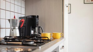 Una cocina con estufa a gas, cafetera y dos tazas amarillas sobre la encimera.