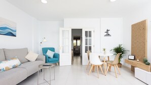 A modern living room with a sofa, a blue armchair, a dining table with chairs, and a kitchen area visible through an open door. - Home2Book Rotia Duplex Caletillas, Terrace (Las Caletillas)