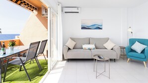 A modern living room with a sofa, a small table, and a blue armchair. There is a balcony with a table and chairs, and an air conditioning unit on the wall. - Home2Book Rotia Duplex Caletillas, Terrace (Las Caletillas)