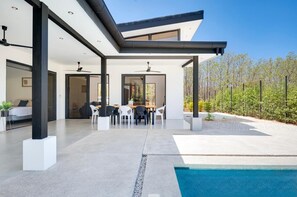 Een modern huis met een overdekt terras, een zwembad en een eethoek met tuinmeubilair.