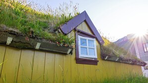 En gul bygning med et lille vindue og et skråt tag dækket af vegetation.