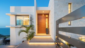 Una casa moderna con puerta de madera, un balcón con sillas y vista al océano.