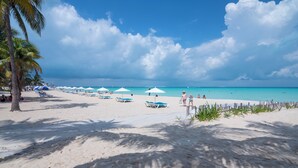 Una playa de arena blanca, palmeras y sombrillas azules.
