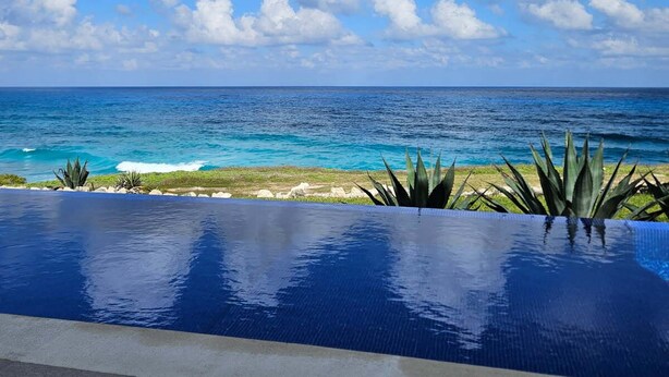 Un cielo azul despejado con nubes, un océano turquesa y una piscina con vista al mar.