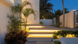 Un edificio moderno con una escalera que conduce a la entrada, rodeado de palmeras y jardines bien cuidados.