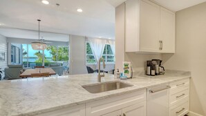 A modern kitchen with a marble countertop, stainless steel sink, and white cabinetry. - Waterfront, Spa/Pool, Private Paradise on Longboat Key! (Longboat Key)