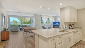 A modern kitchen with a marble countertop, white cabinetry, and a dining area with a wooden table and chairs. - Waterfront, Spa/Pool, Private Paradise on Longboat Key! (Longboat Key)
