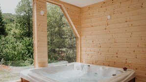Une cabane en bois avec un bain à remous, une fenêtre et une vue sur la forêt.