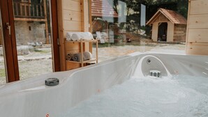 Un bain à remous avec un banc en bois et des serviettes, entouré d’un chalet en bois et d’un mur de pierres.