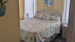 Een slaapkamer met een bed, een plafondventilator, een raam met gordijnen en een ingelijst schilderij aan de muur.