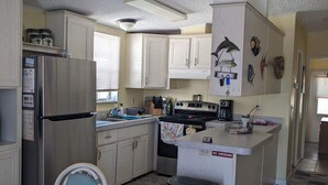 Een kleine keuken met witte kastjes, een koelkast, een fornuis en een eethoek met een tafel en stoelen.