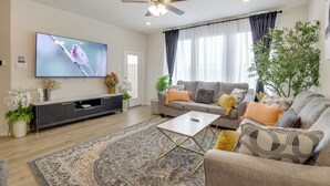Uma sala de estar moderna com televisão de tela plana, ventilador de teto, conjunto de sofás, mesa de centro e um tapete decorativo.