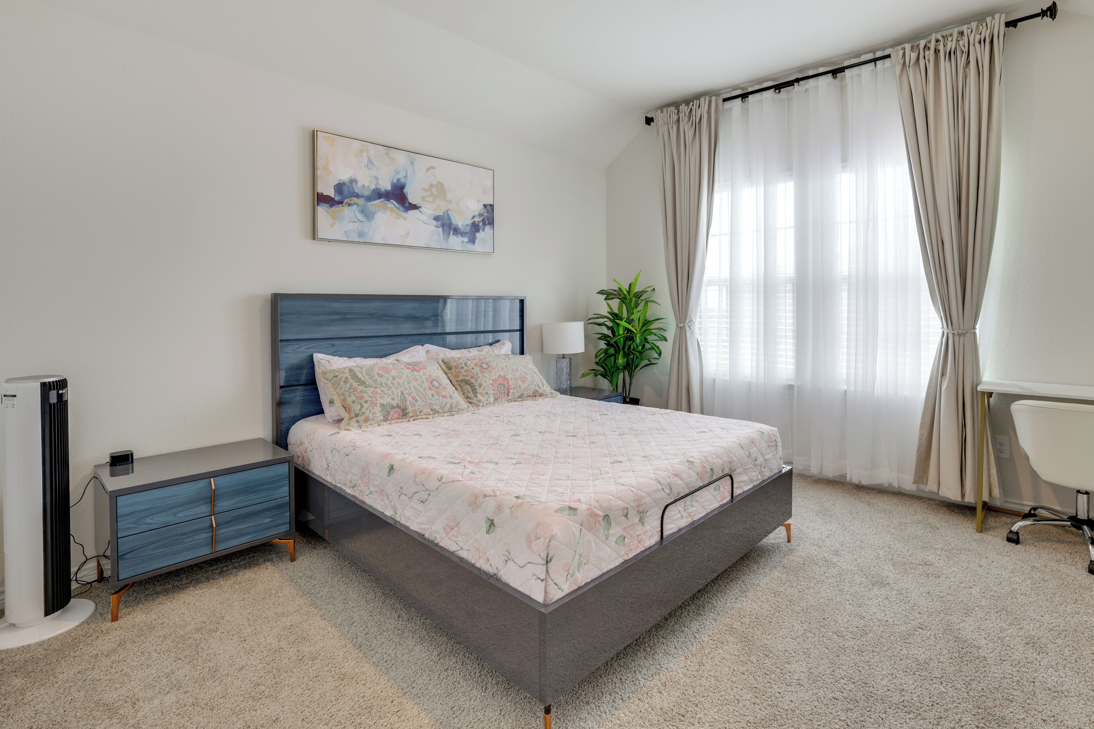 A modern bedroom with a bed, bedside table, lamp, and a potted plant.