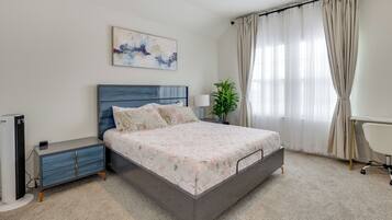 A modern bedroom with a bed, bedside table, lamp, and a potted plant.