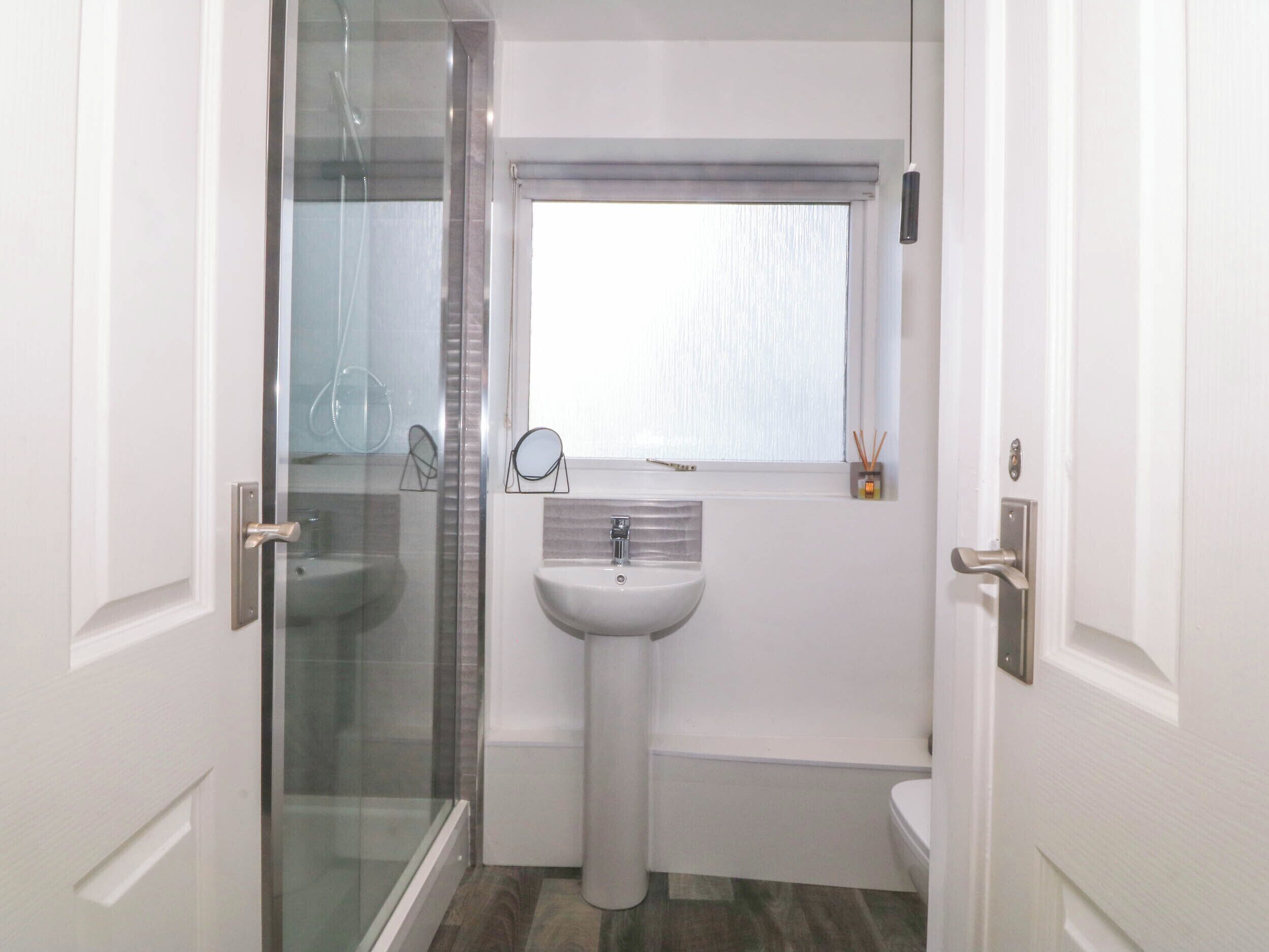 A compact bathroom with a glass shower enclosure, a pedestal sink, and a toilet.