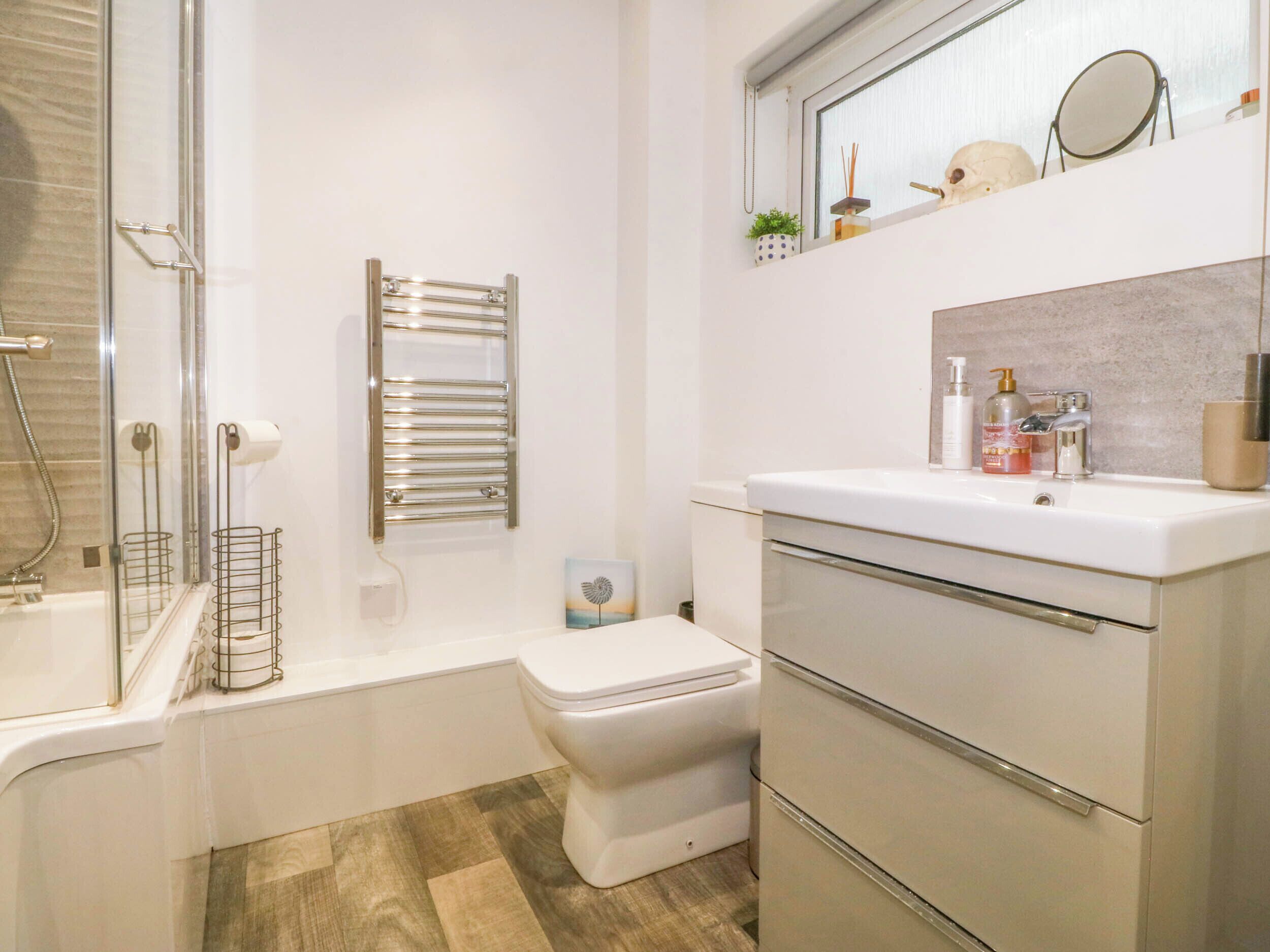A modern bathroom with a glass shower enclosure, a white toilet, a built-in sink with a mirror, and a towel rack.
