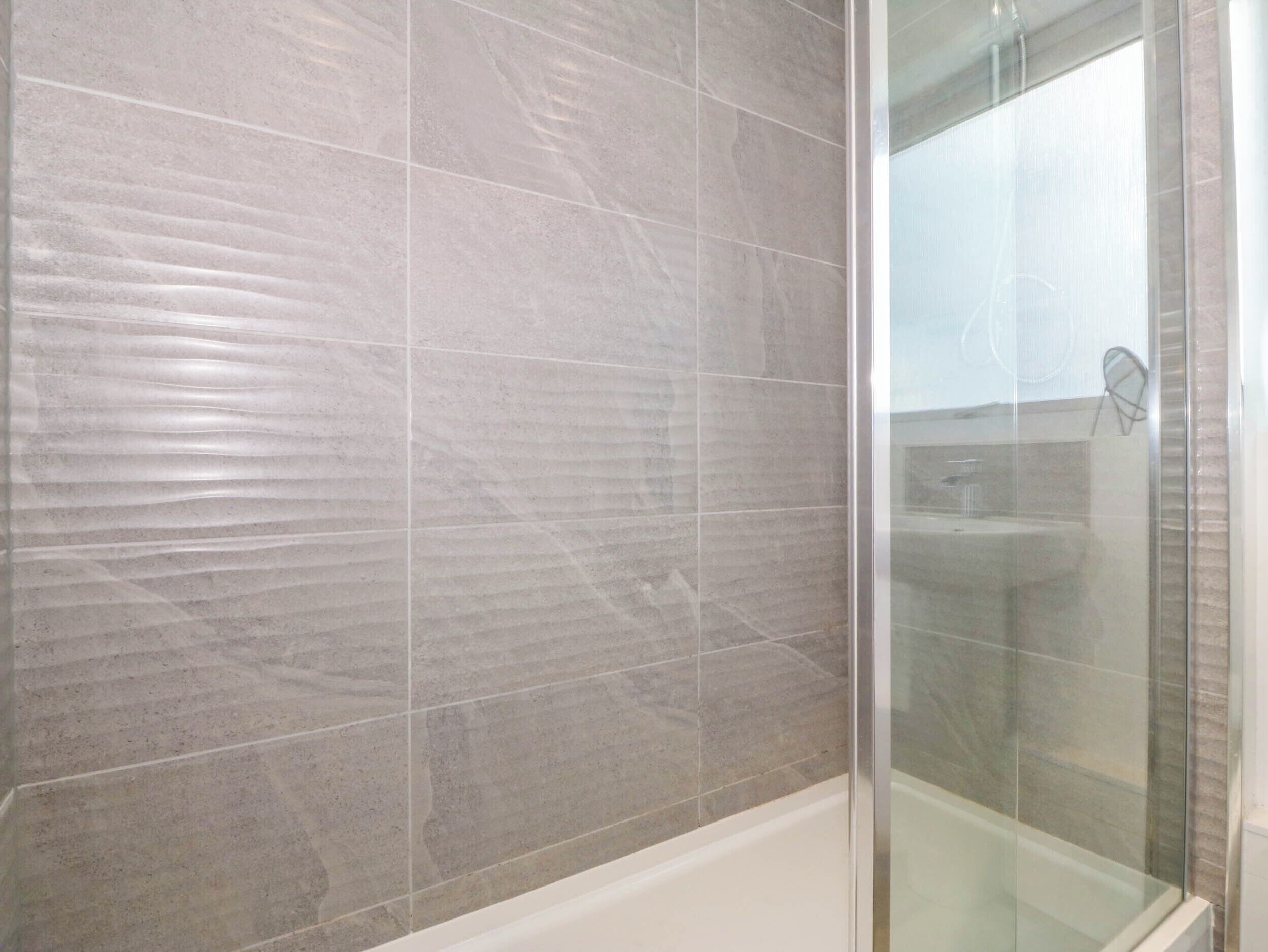 Un baño moderno con cabina de ducha de vidrio y paredes con azulejos grises.