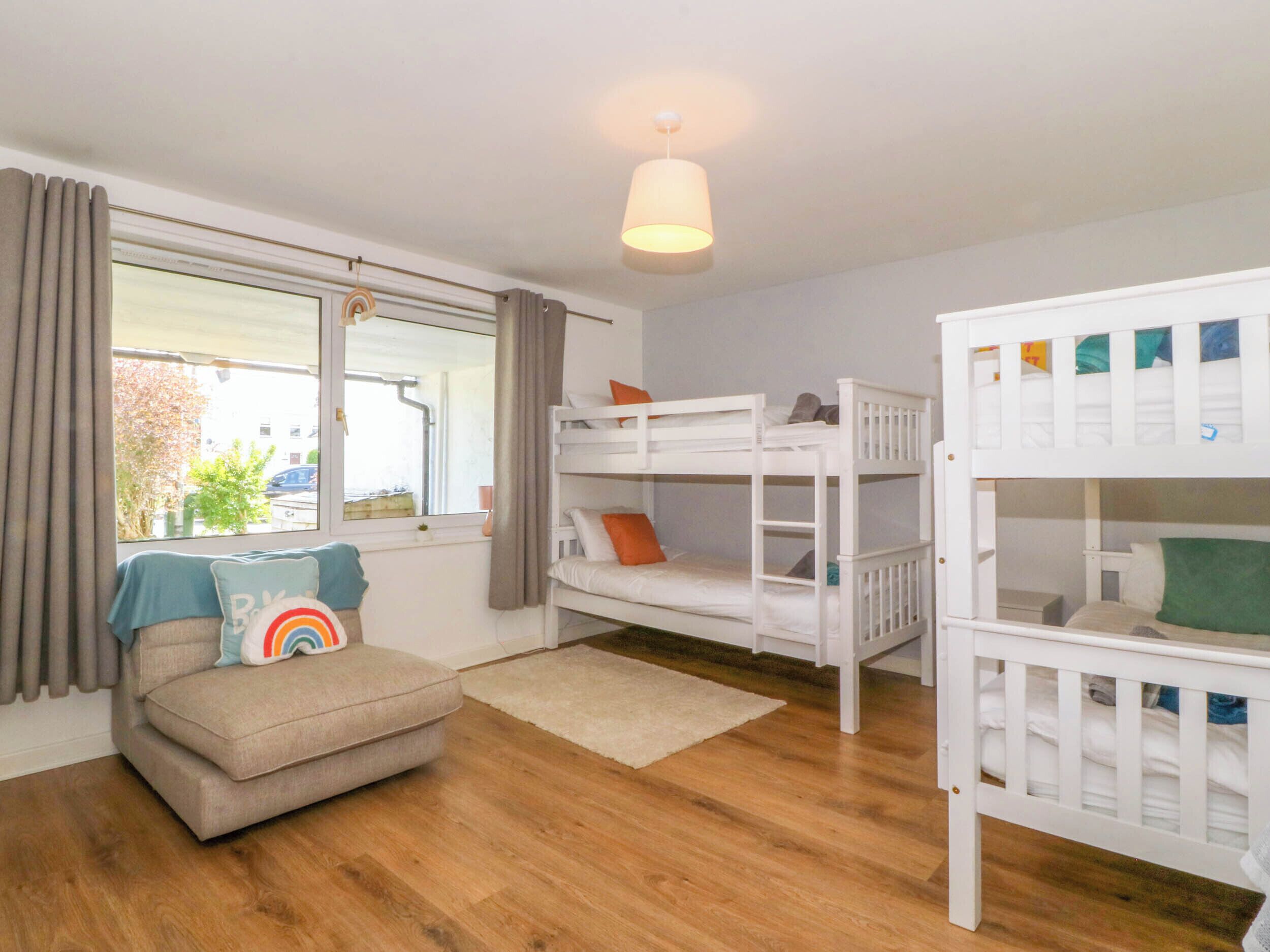 A room with a sofa, two bunk beds, a window with curtains, and a ceiling light.
