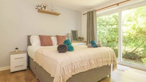 A bedroom with a bed, a nightstand, a dresser, a window with curtains, and a view of greenery outside. - Ty Golau (Pwllheli)