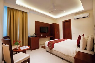 Una habitación de hotel con cama, escritorio, silla, televisor y armario.