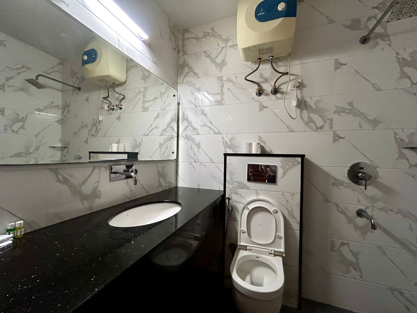 A bathroom with a black countertop sink, a mirror, a toilet, and a hand dryer.