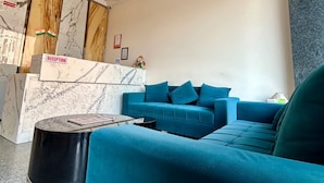 A reception area with a marble counter, a teal sofa, and a black round table. - Z Suites Hotel Mahipalpur IGI Airport (New Delhi)