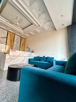 A reception area with a marble counter, a teal sofa, and a black round table. - Z Suites Hotel Mahipalpur IGI Airport (New Delhi)