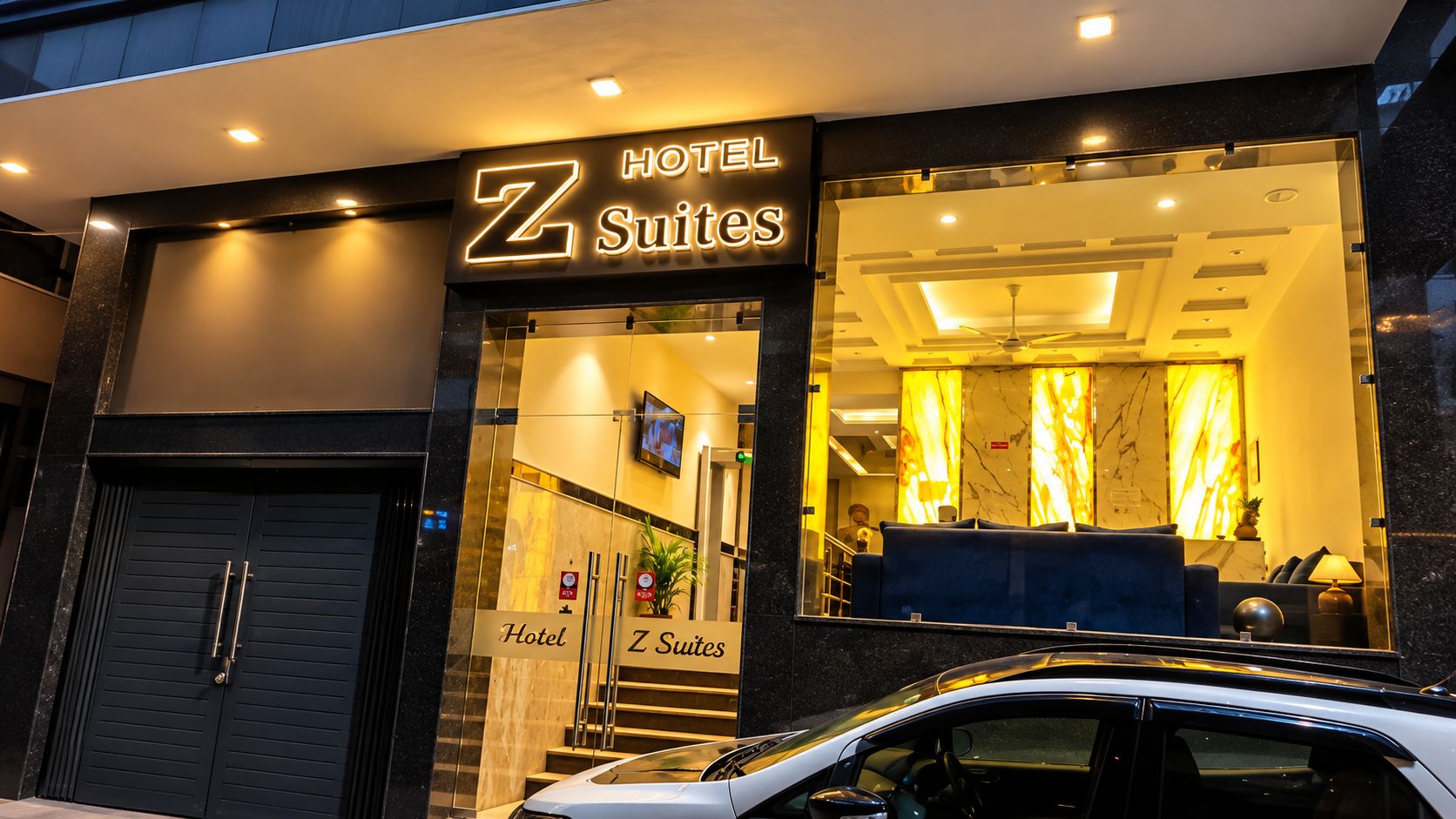 A hotel entrance with a sign for 'Z Suites' and a visible reception area with a seating arrangement.