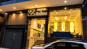 Entrada de hotel con un letrero que dice 'Z Suites' y una recepción visible con un área de descanso.
