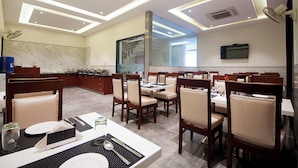 A modern dining area with wooden chairs and tables, a large mirror, and a TV on the wall. - Z Suites Hotel Mahipalpur IGI Airport (New Delhi)