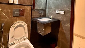 A bathroom with a toilet, sink, and mirror. There is a hairdryer on the wall and a showerhead. - Z Suites Hotel Mahipalpur IGI Airport (New Delhi)