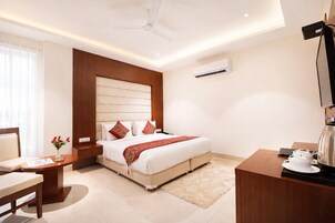 A hotel room with a bed, bedside table, chair, desk, and a television.