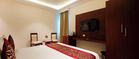 A hotel room with a large bed, a TV mounted on the wall, a ceiling fan, and a wooden wardrobe.
