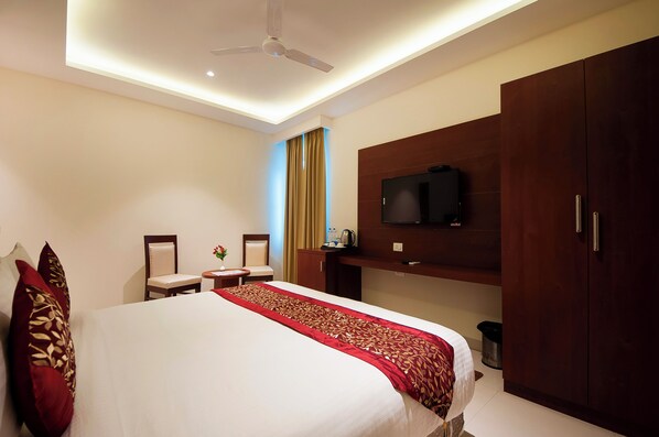 Habitación de hotel con una cama grande, un televisor montado en la pared, un ventilador de techo y un armario de madera.