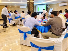 Una sala conferenze con tavoli rotondi, sedie con nastri azzurri e partecipanti seduti.