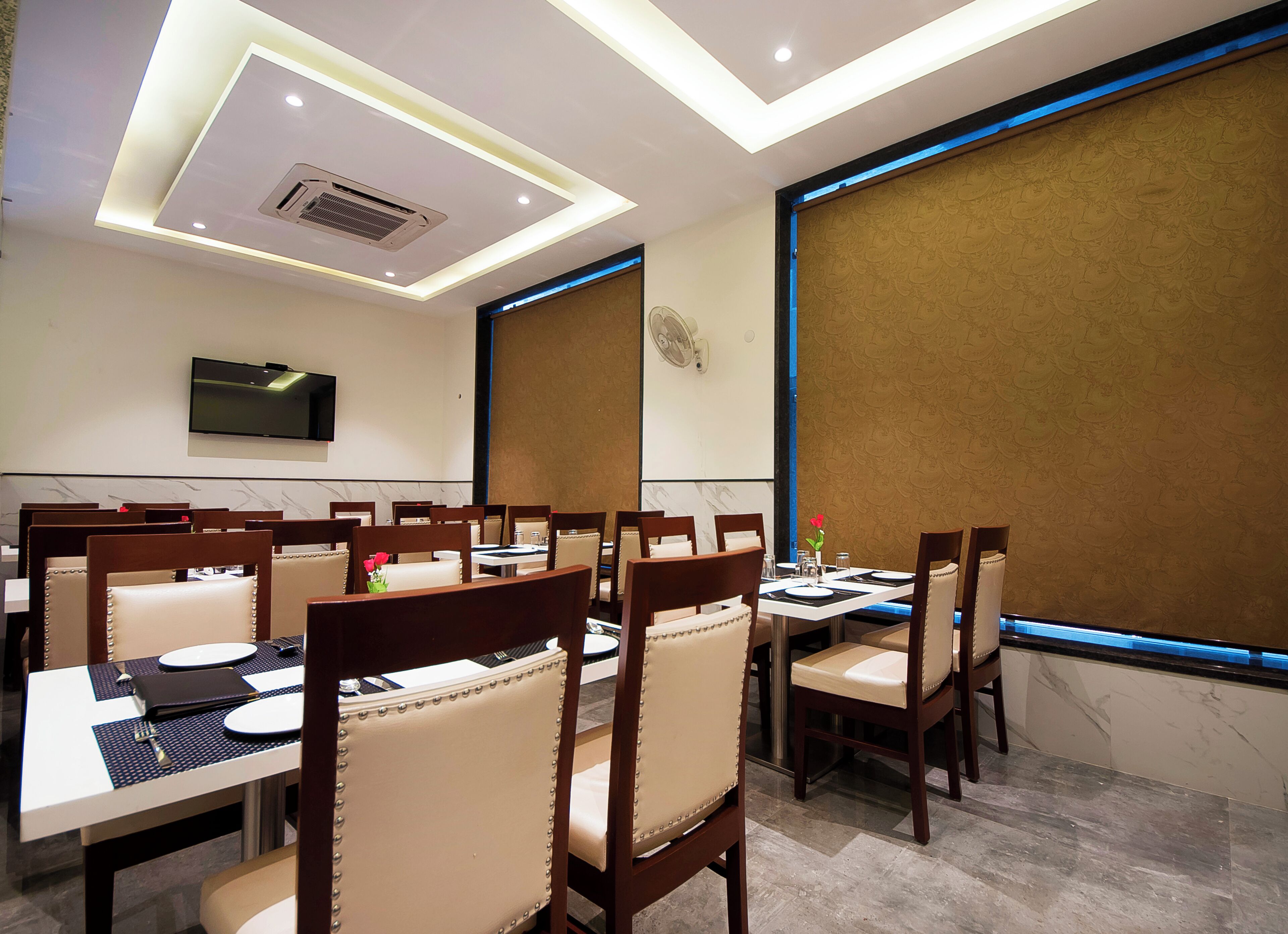 Une salle à manger d’hôtel avec plusieurs tables et chaises, un téléviseur à écran plat fixé au mur et un paravent décoratif sur le mur du fond.