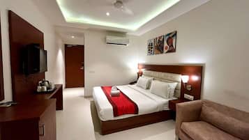 A hotel room with a bed, a TV, a desk with a coffee maker, a couch, and artwork on the wall.