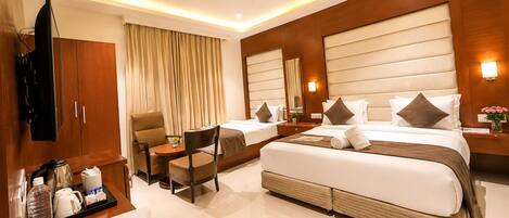 A hotel room with a bed, two chairs, a desk with a sign, a television, and a ceiling fan.