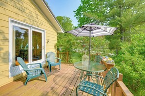 Une terrasse en bois avec une table et des chaises en verre, un parasol et une cage à oiseaux.