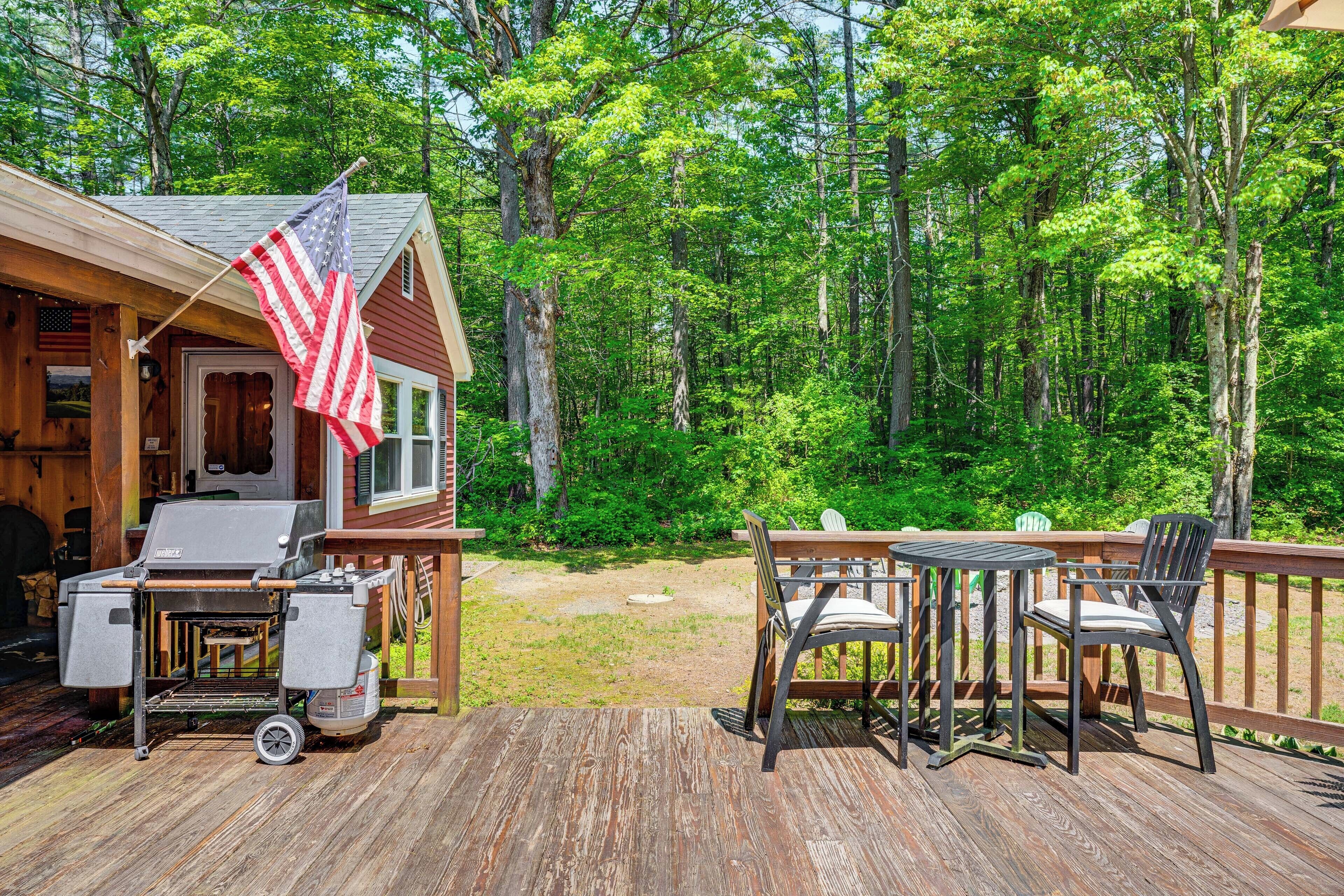 A wooden cabin with a grill and outdoor seating area, surrounded by a forest.
