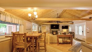Un salón amplio con techo de madera, chimenea, televisor y comedor con mobiliario de madera.