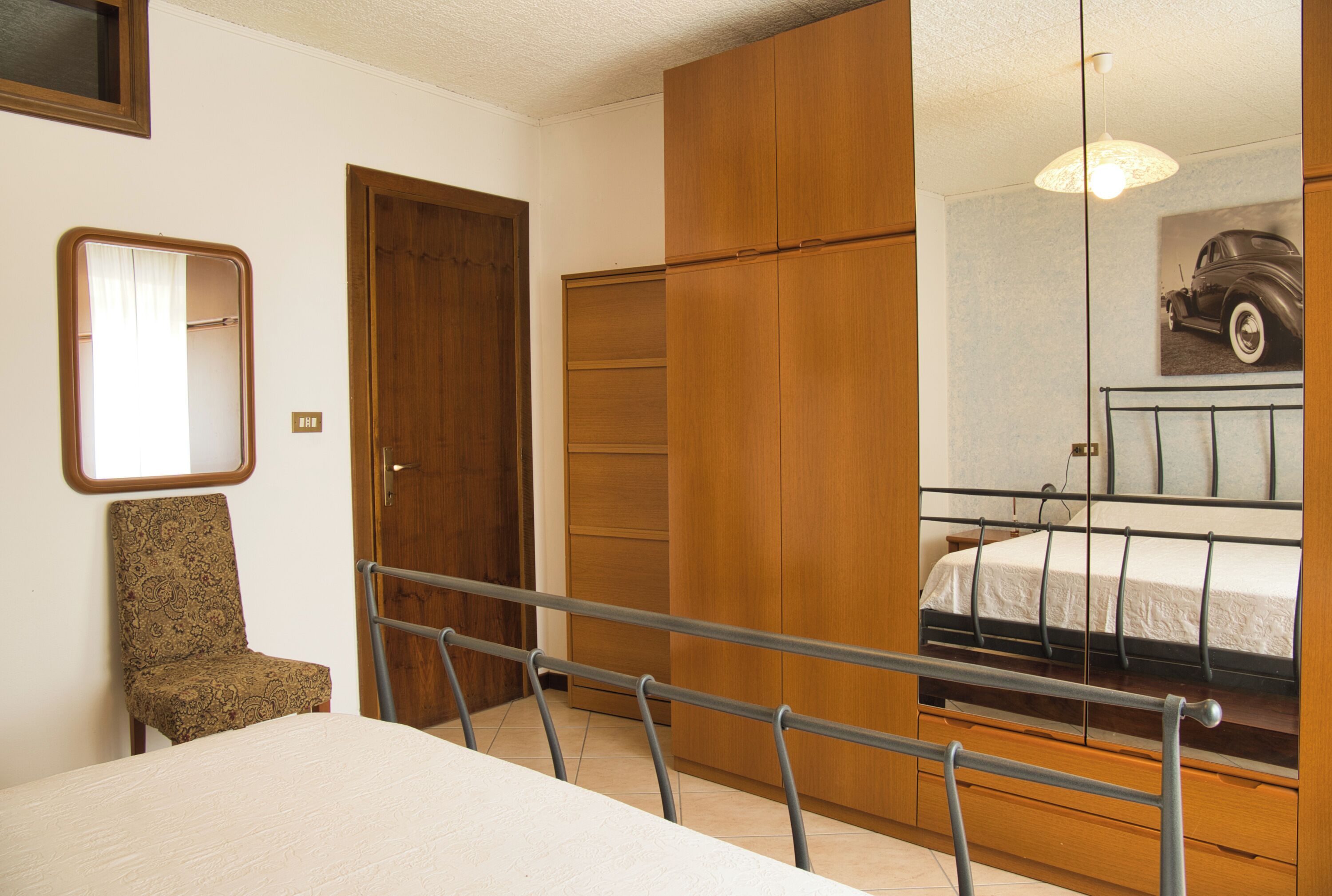 Un dormitorio con cama, una silla, un armario y un espejo.